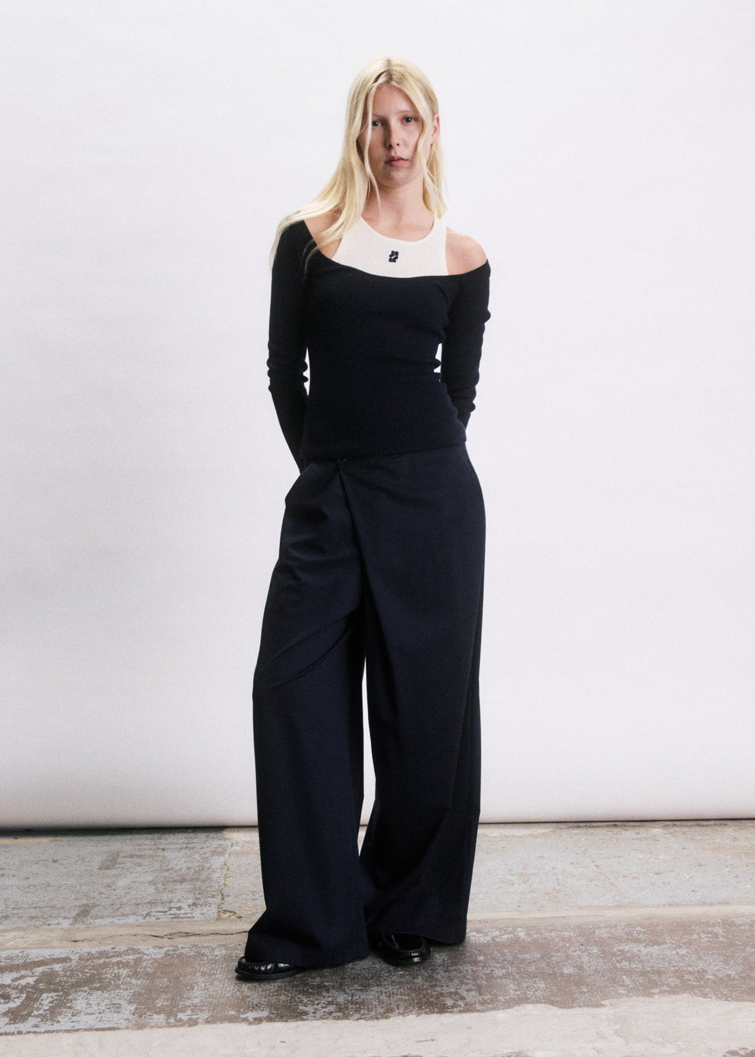 Modèle porte le Pull Vance JIJI Studio, un haut bleu marine épaules dénudées sur débardeur blanc, avec pantalon large marine.